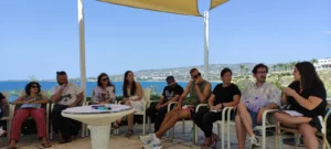 Participants of the EU Teams for EU Dreams training course sitting outdoors by the sea during a non-formal learning session in Paphos.