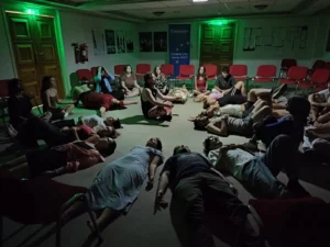 Participants lying on the floor in a dim room with green lighting during a guided meditation and relaxation activity.