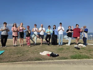 Group of young people posing in tree pose during a morning mindfulness and yoga session overlooking the sea in Paphos.