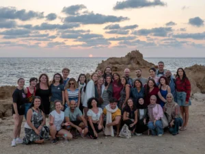 Participants of the YETF photography training course posing together by the seaside at sunset, captured during a Photovoice field session.